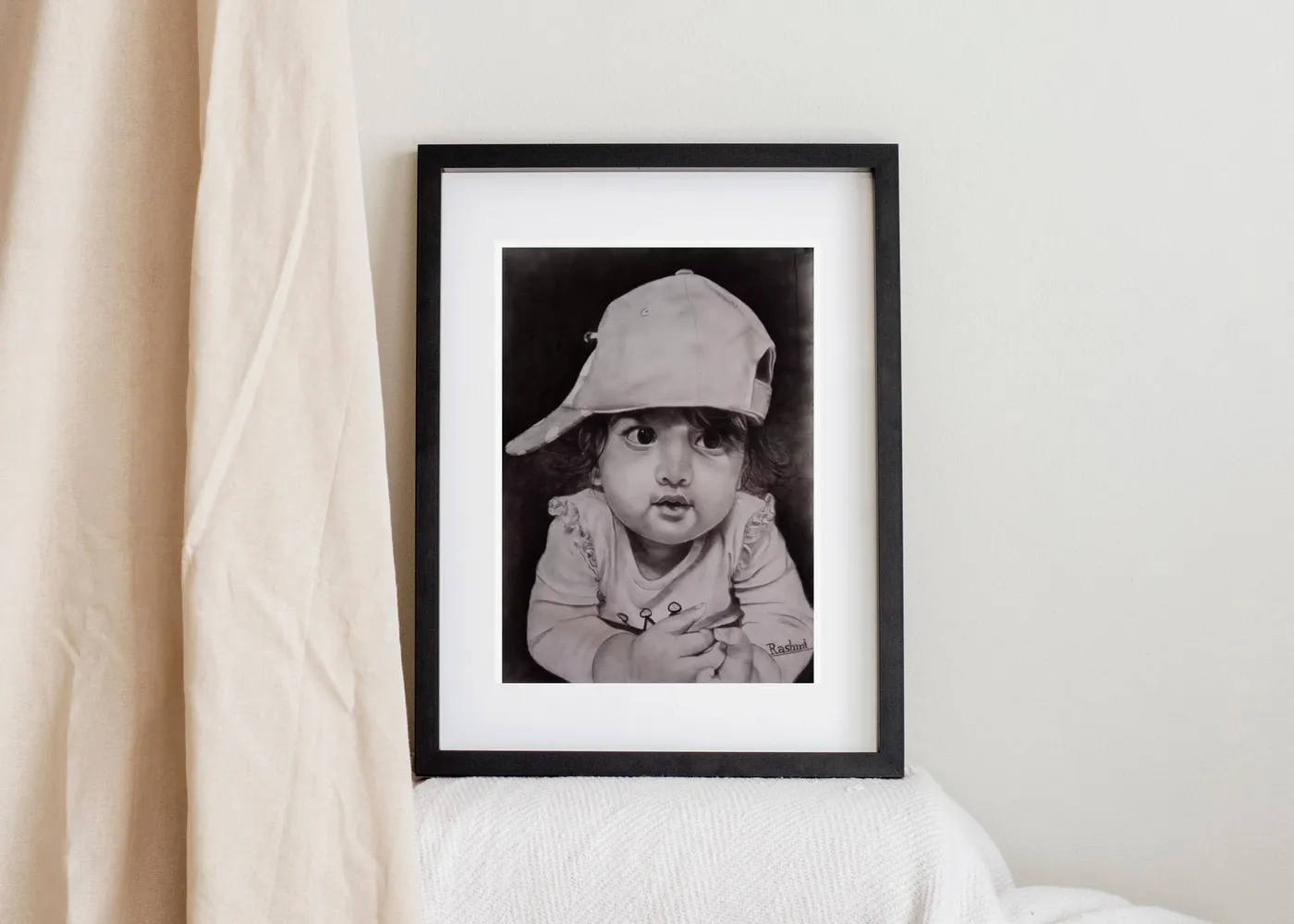 Hand-drawn charcoal portrait of a child in a black frame beside a linen curtain