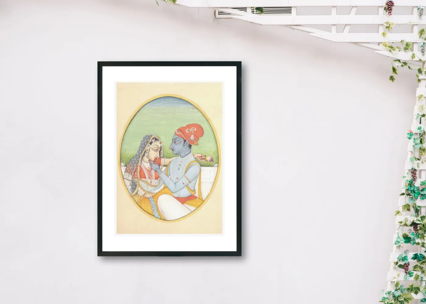 Radha Krishna miniature painting in a black frame on a white wall with plants
